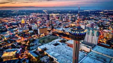Aerial view of downtown San Antonio, Texas at night with rotating Tower of the Americas in foreground.
